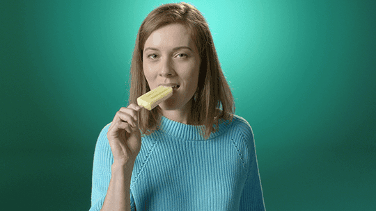 Frau ist ein gelbes Capri Eis und lächelt.